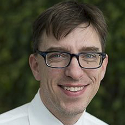 a person with short dark hair and a white shirt and glasses